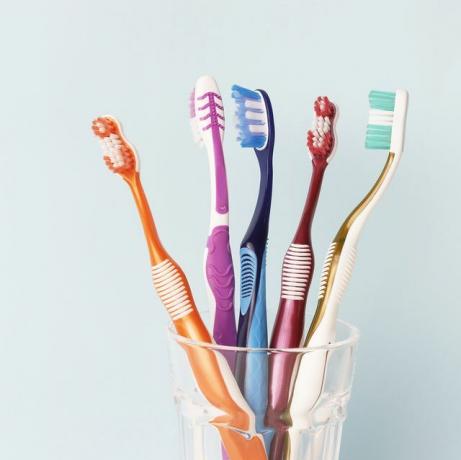 flerfarvede tandbørster i en glaskop, blå baggrund