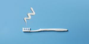 nærbillede af en flad liggende hvid tandbørste og tandpasta på blå baggrund